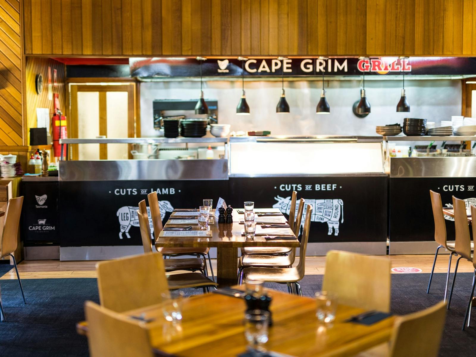 Open part of kitchen with 'Cape Grim Grill' signage above & Kauri Bistro tables in foreground
