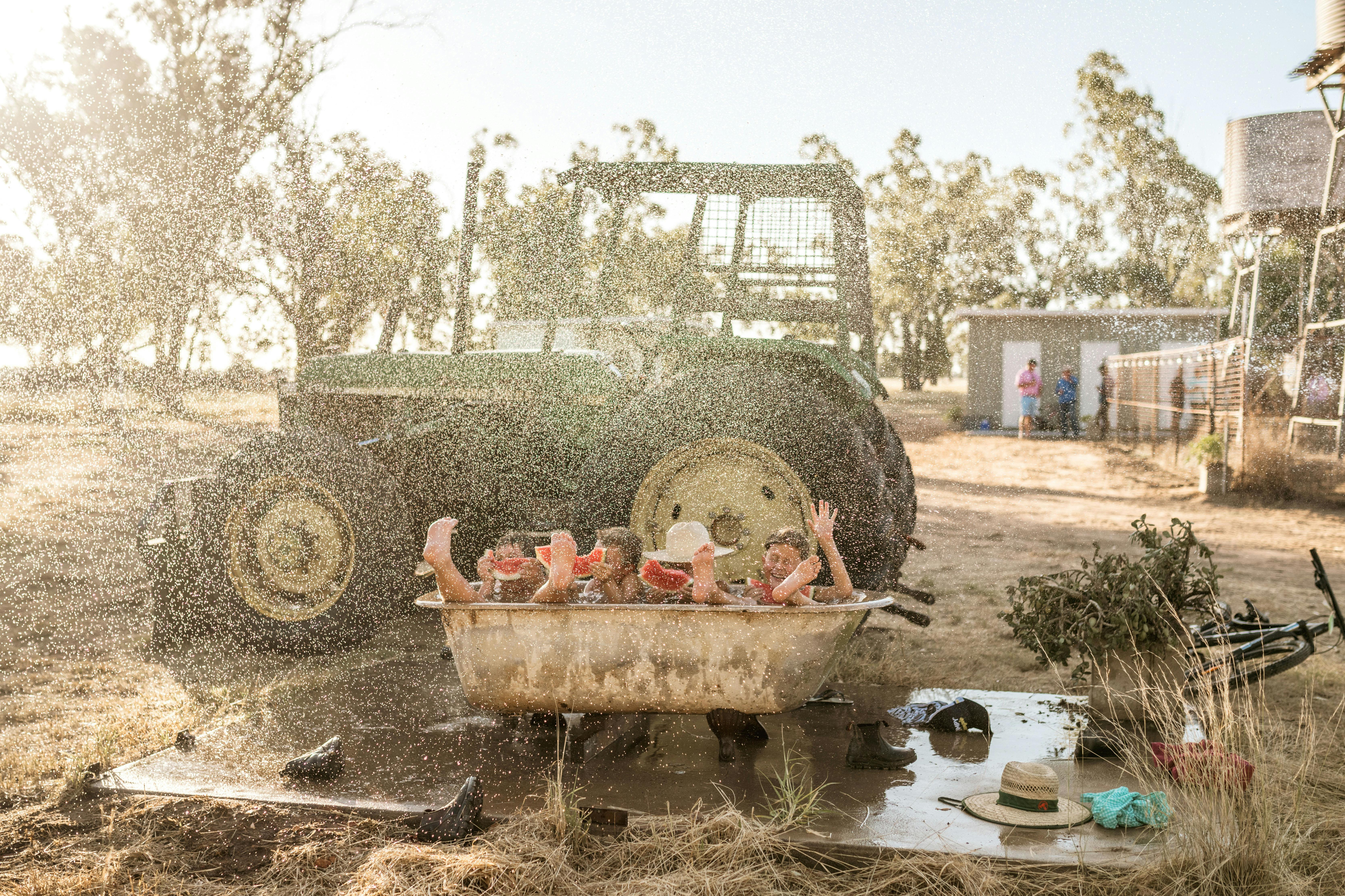 children playing in an outdoor bath in front of an old green tractor in a farm paddock