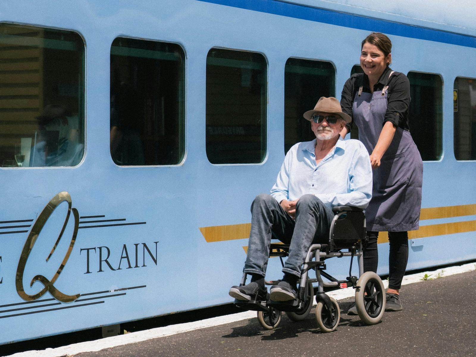 The Q Train waiter pushing a gentleman on a wheelchair next to The Q Train