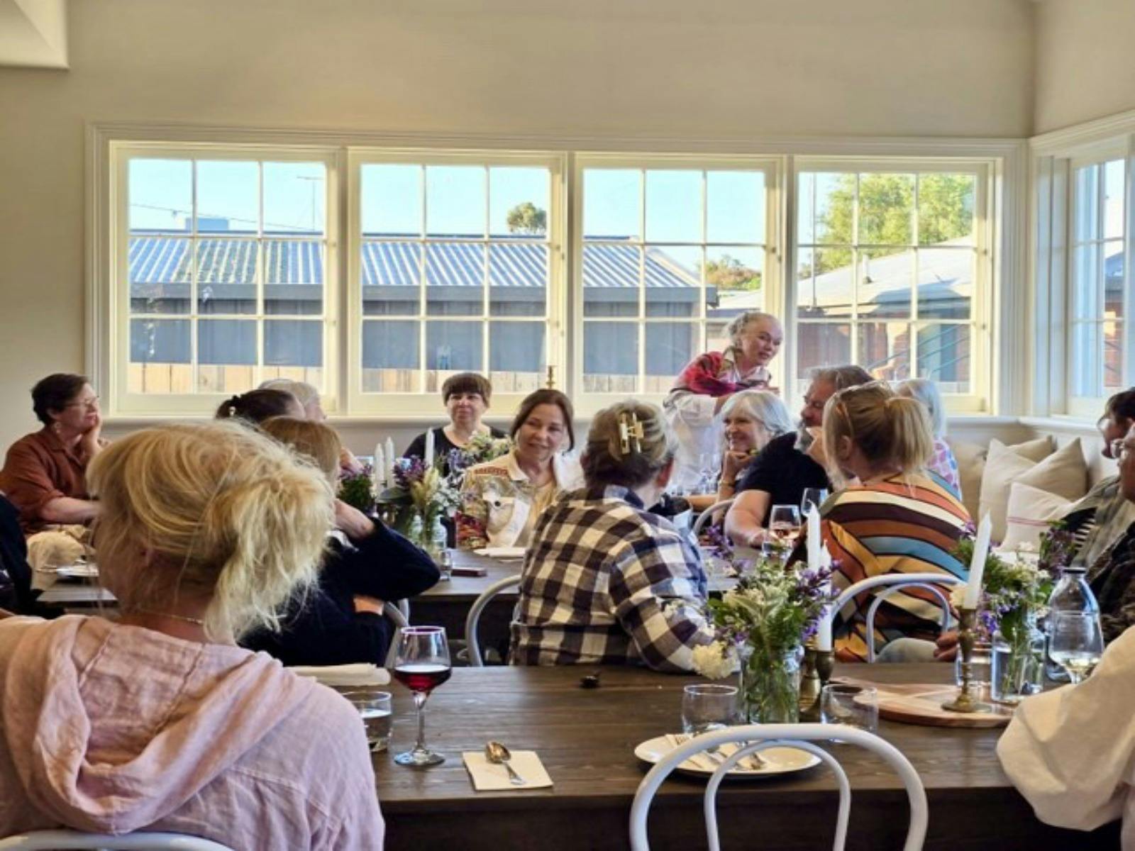 A group of people sit in a dining room with drinks, sitting, smiling and talking