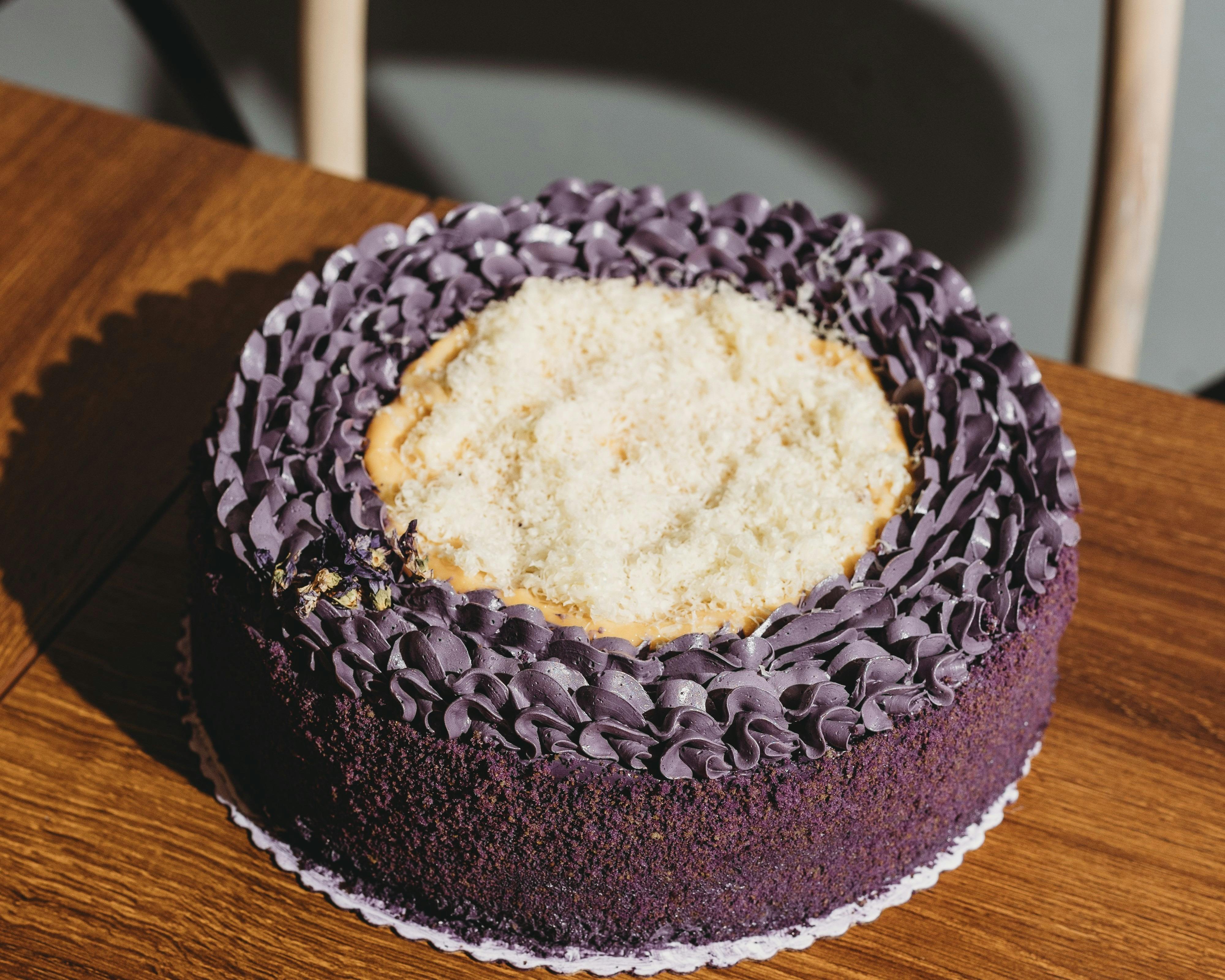 A round ube cake with purple frosting and a light shredded topping, placed on a wooden surface.
