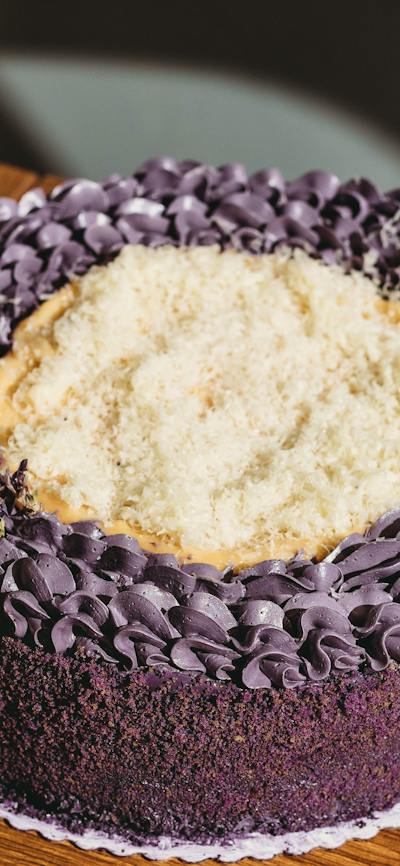 A round ube cake with purple frosting and a light shredded topping, placed on a wooden surface.