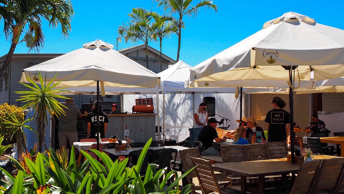 The Grounds Collective's outdoor garden dining area with shaded tables, trees and umbrellas