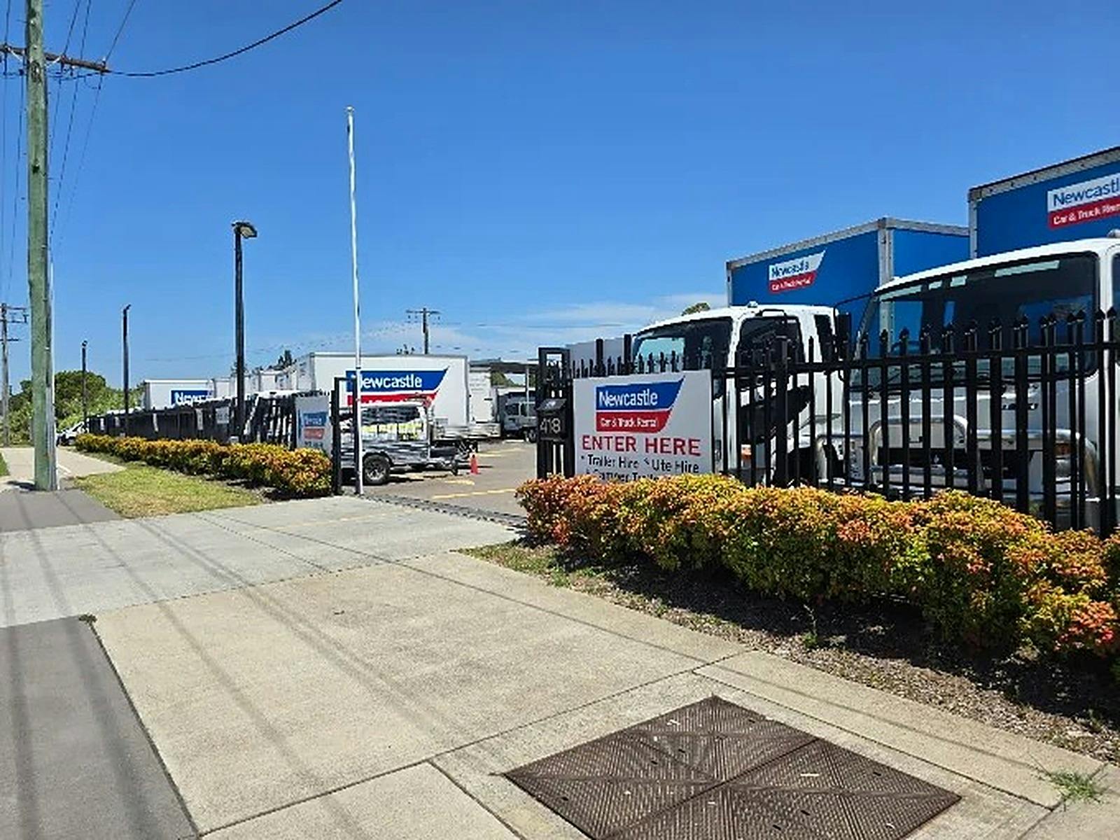 Row of Newcastle Car & Truck Rental trucks and a trailer behind a black fence