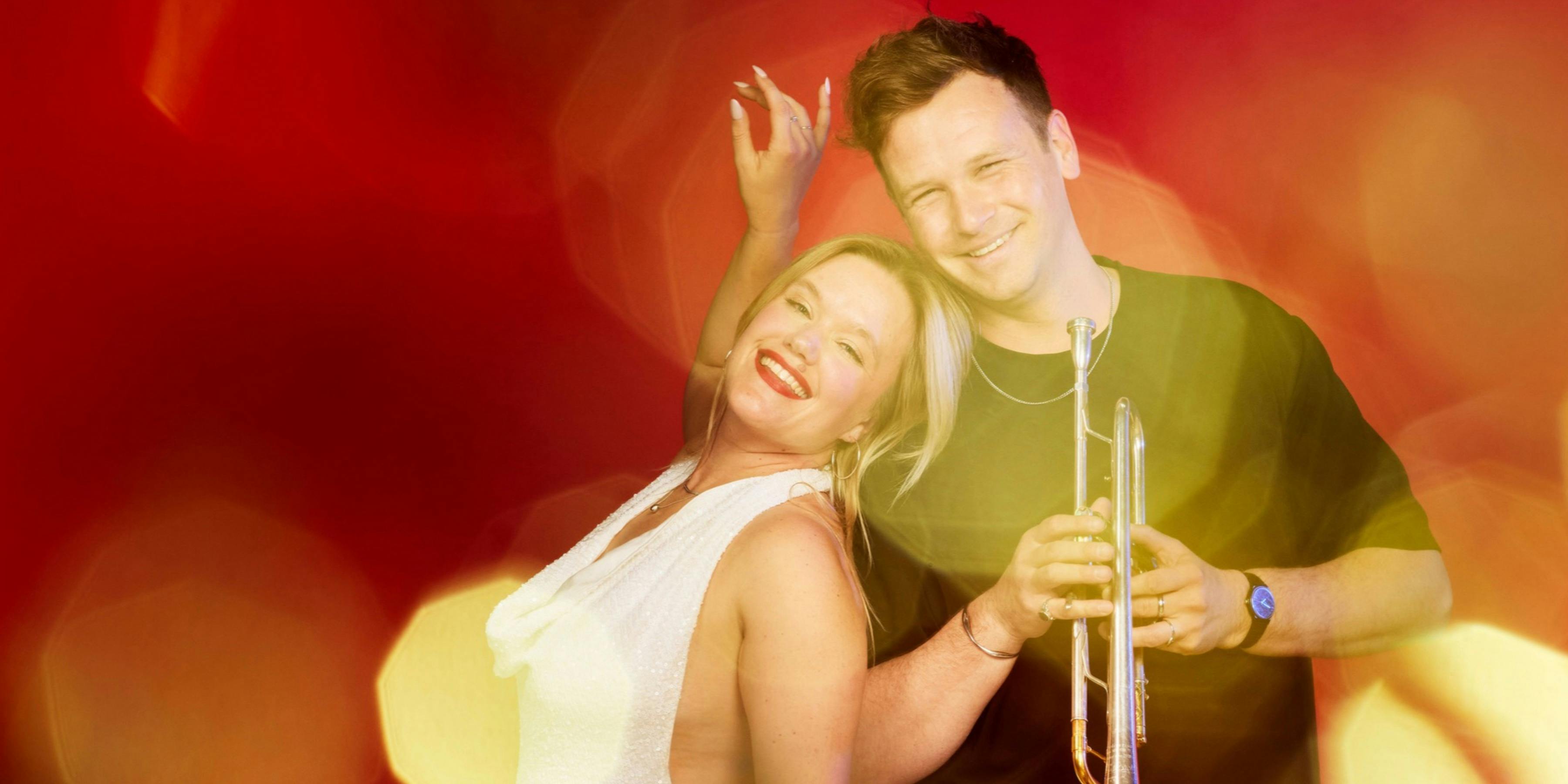 Rachel Mink - Soprano and Alex Raupach - Trumpet pose in front of a Christmas red background