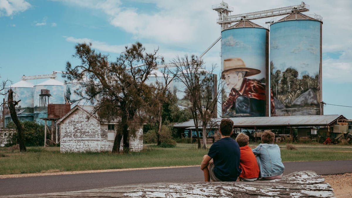 Three kids sitting on a log, admiring the Yelarbon Silos