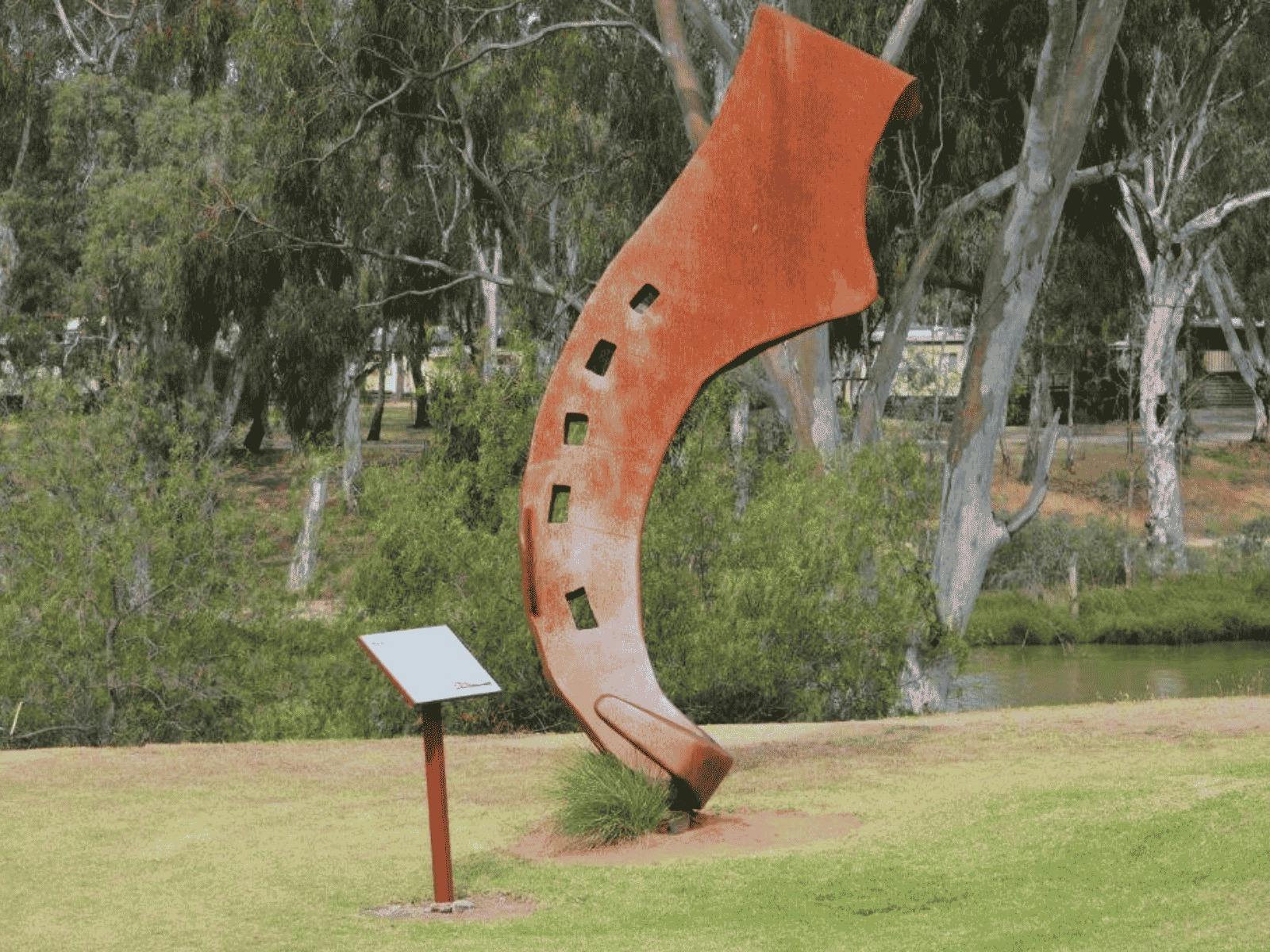 A rusted metal sculpture stands in a park