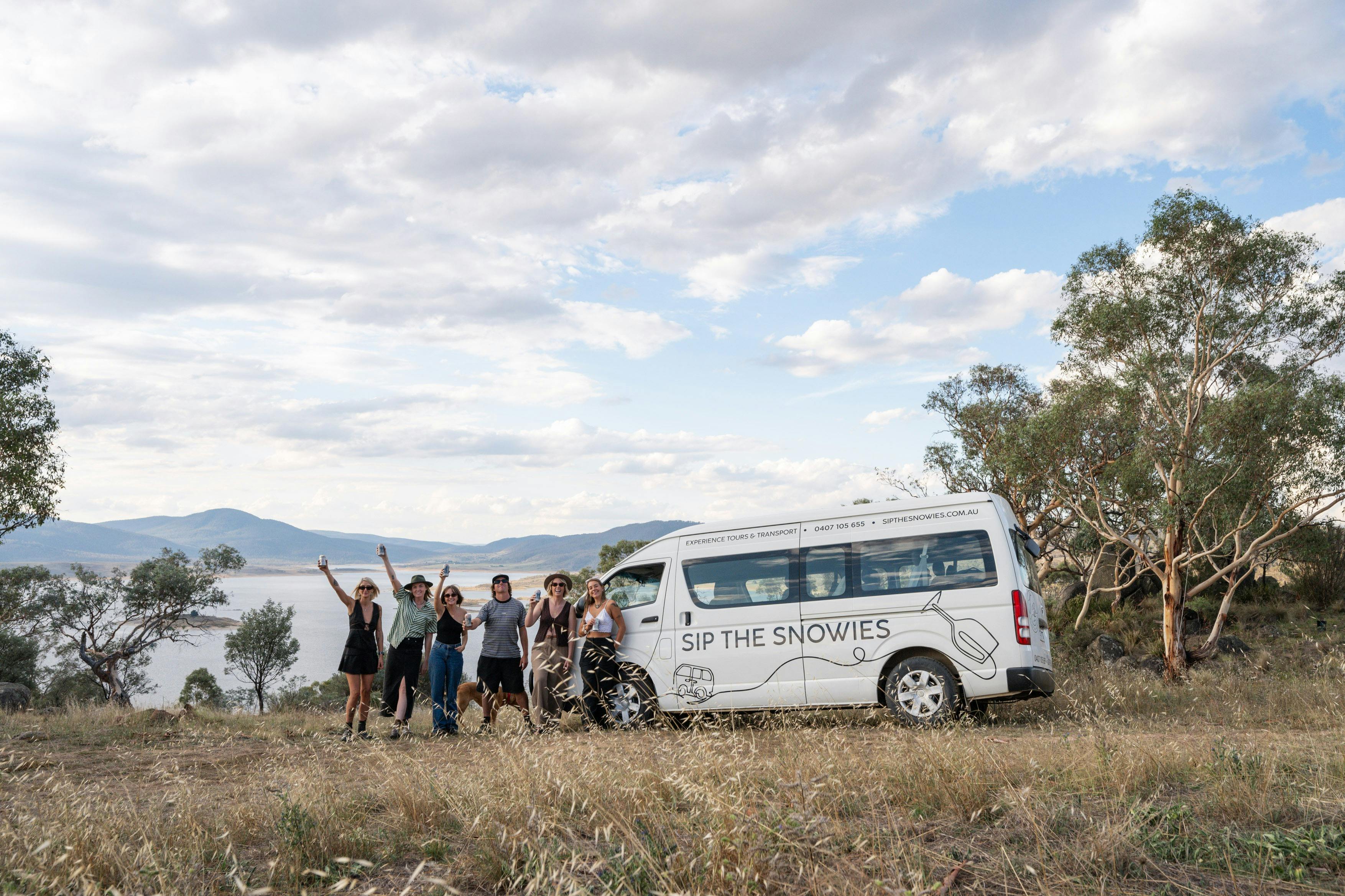A group of 5 tour guests enjoying the view and scenery of Lake Jindabyne standing  by the tour bus