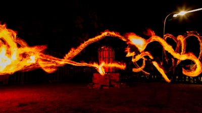 A long-exposure photo of fire twirlers in front of a glowing red, domed kiln.