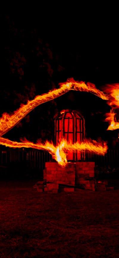 A long-exposure photo of fire twirlers in front of a glowing red, domed kiln.