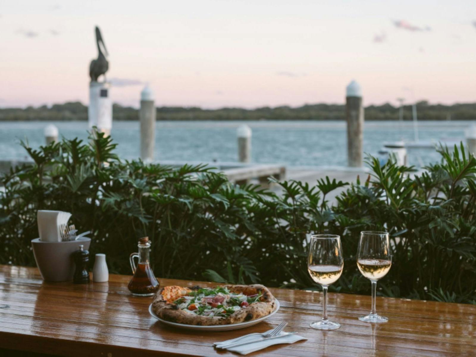 pizza and wine on timber table with river and wharf in background