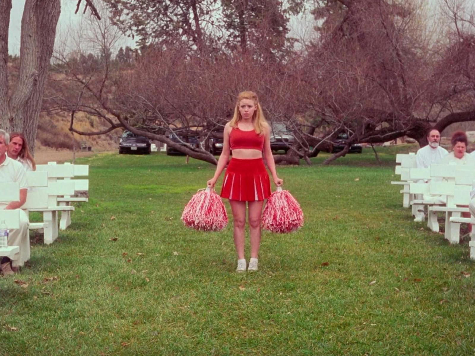 Cheerleader stands between white seating arrangement on green grass