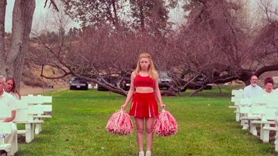 Cheerleader stands between white seating arrangement on green grass