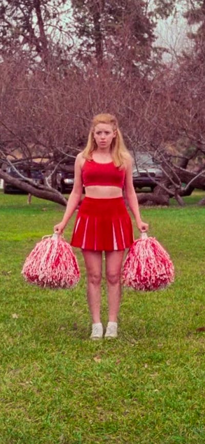 Cheerleader stands between white seating arrangement on green grass