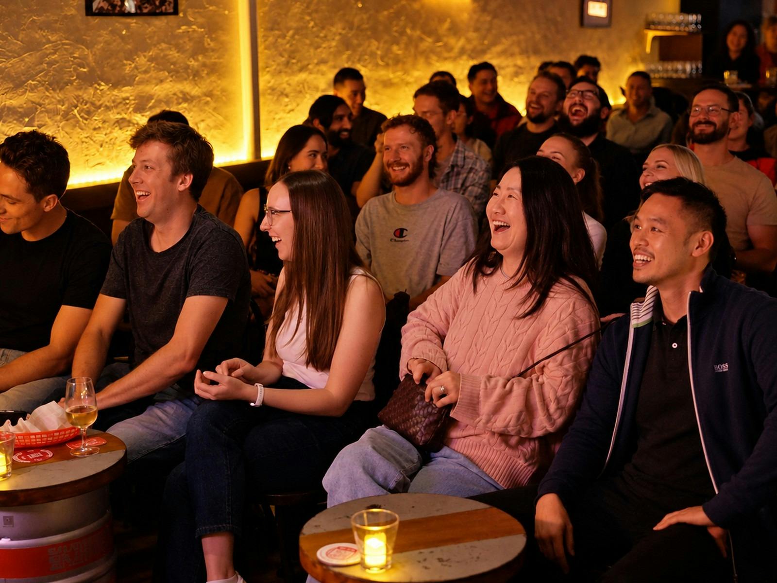 Audience members laughing at a stand-up comedy show in a dimly lit bar