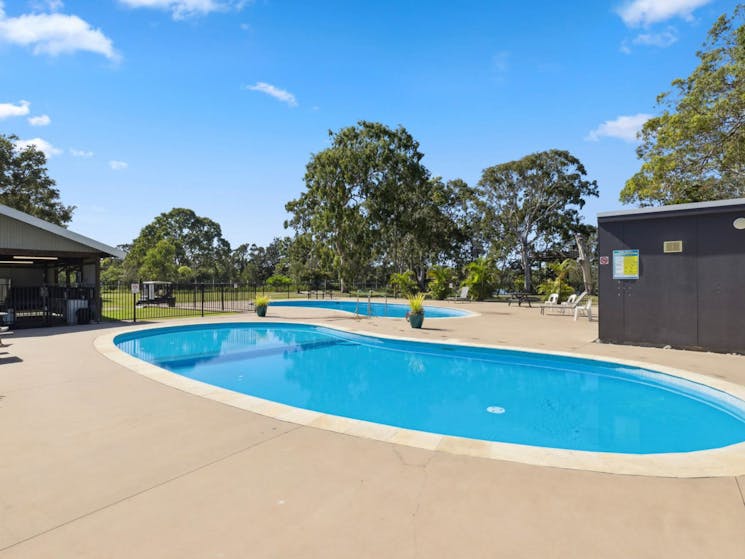 Image of 2 kidney shapped pools. Large gum trees agains a blue sky in the background.