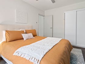 Bedroom with orange bedding, ceiling fan, built-in robe, and sliding door to rear garden.