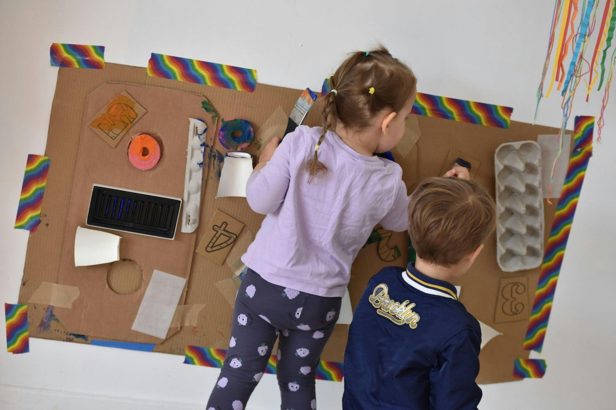 2 small children exploring a textured cardboard paint wall