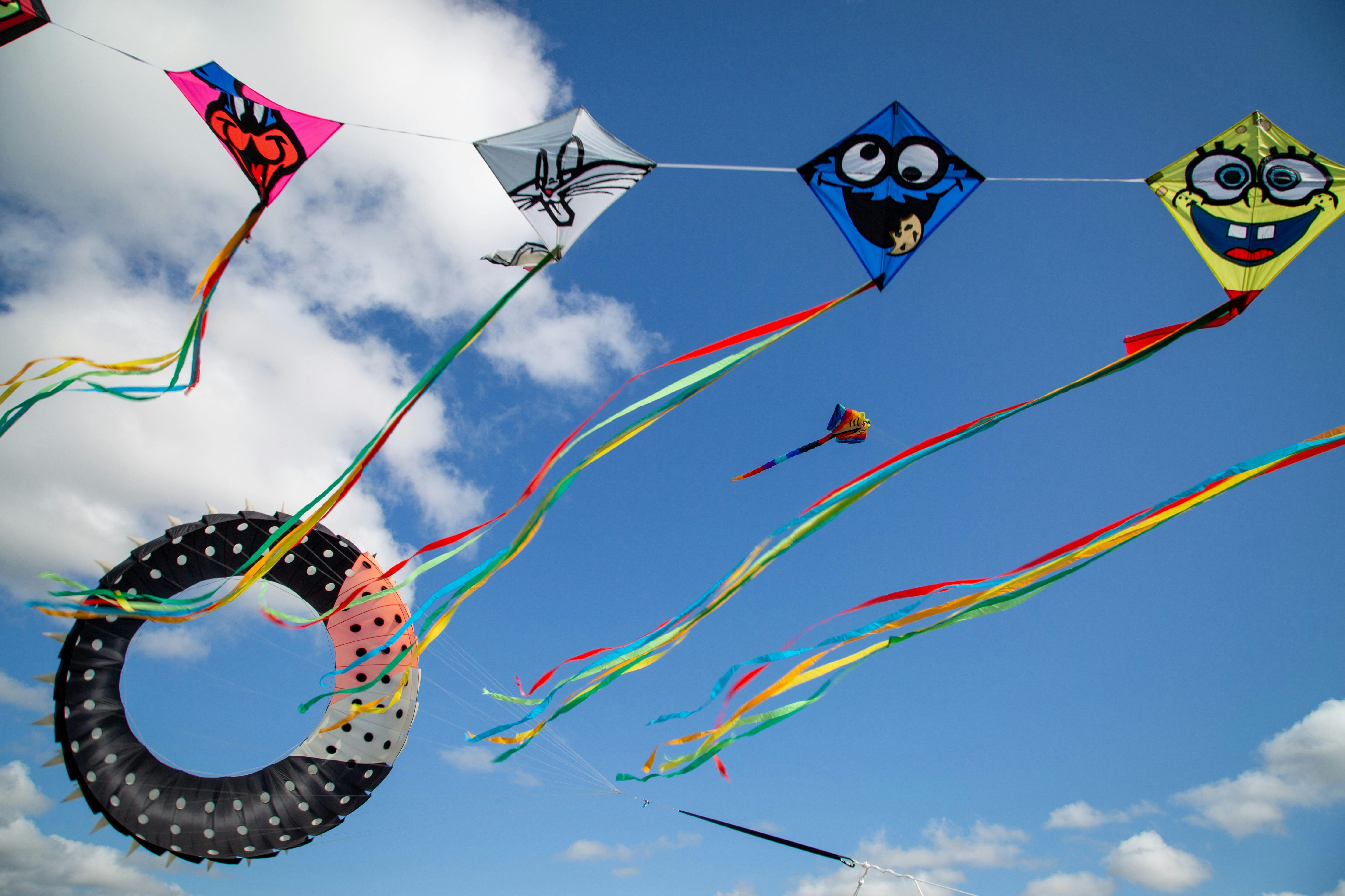 A collection of small and large kites flying in the blue sky.