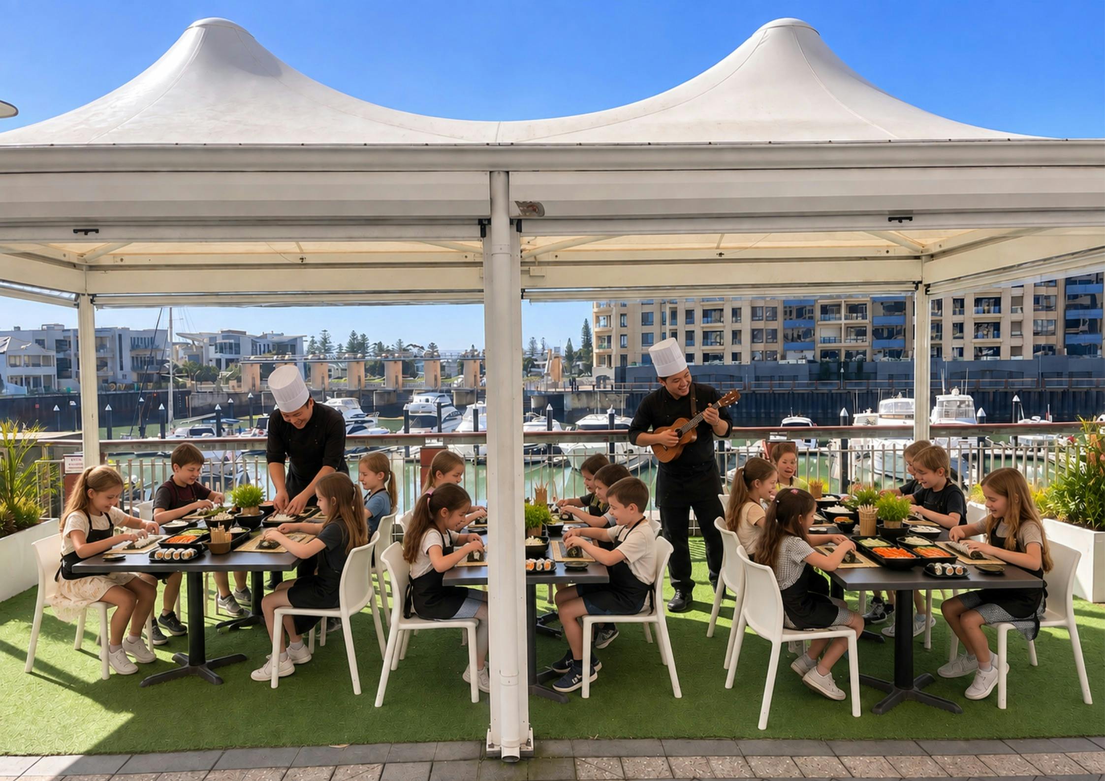A group of kids sitting down making sushi with 2 chefs in front of the marina pier