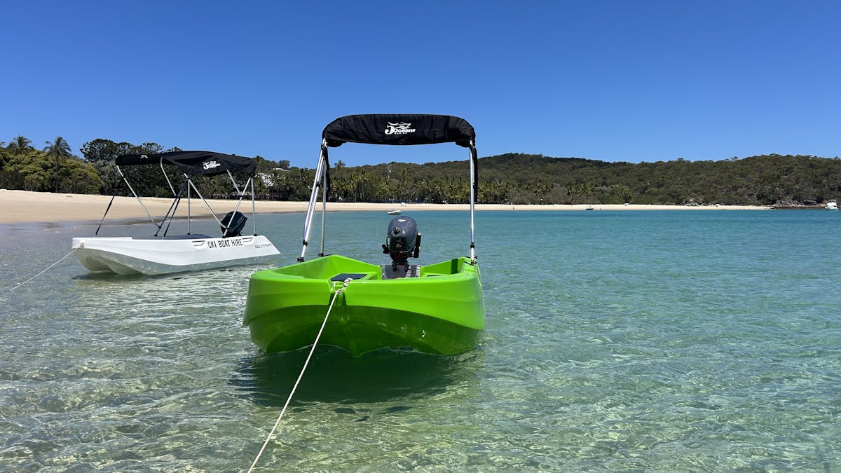 Green and white Polycraft boats anchored in shallow turquoise water at Great Keppel Island.