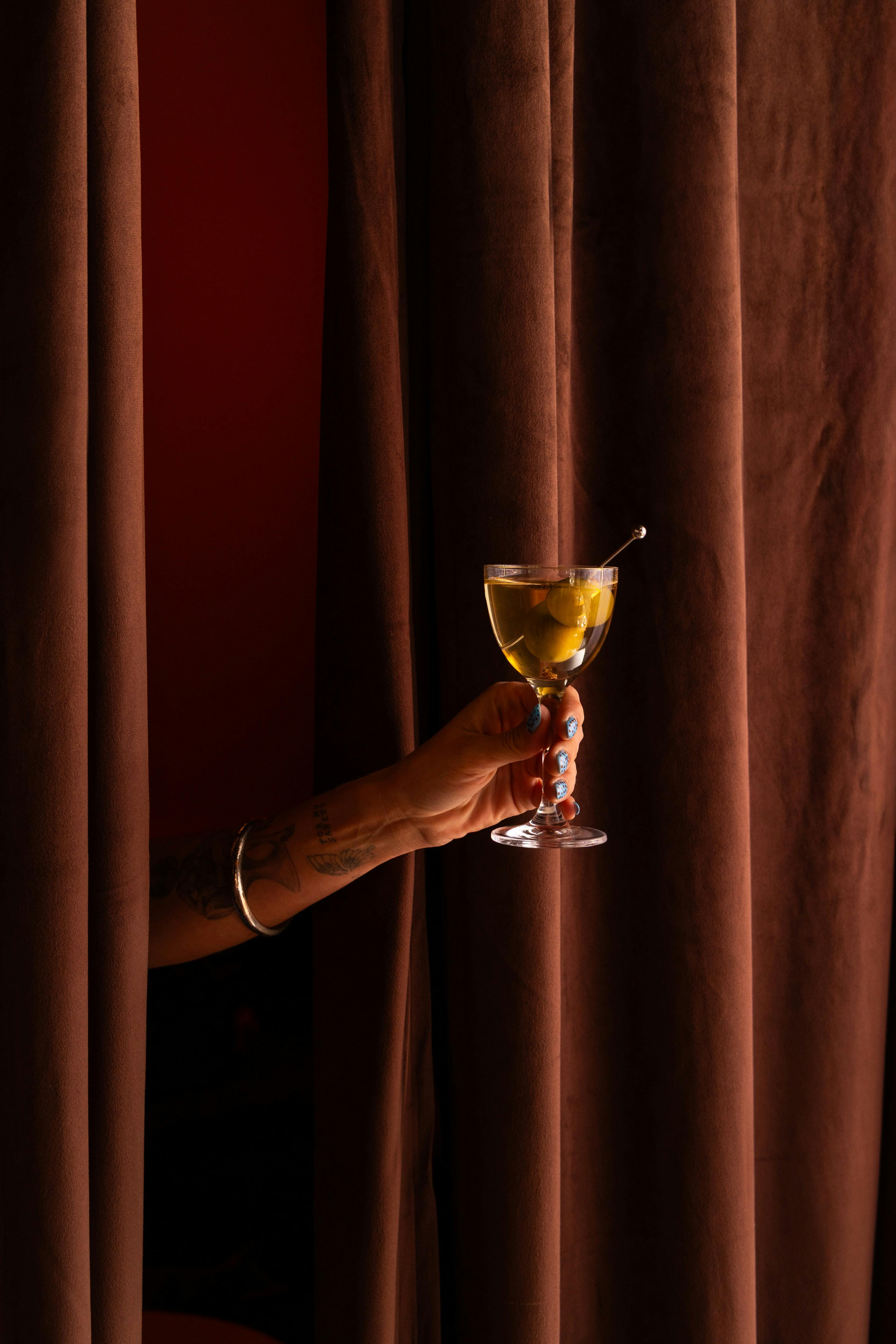 Reaching through curtains holding dirty martini with olives