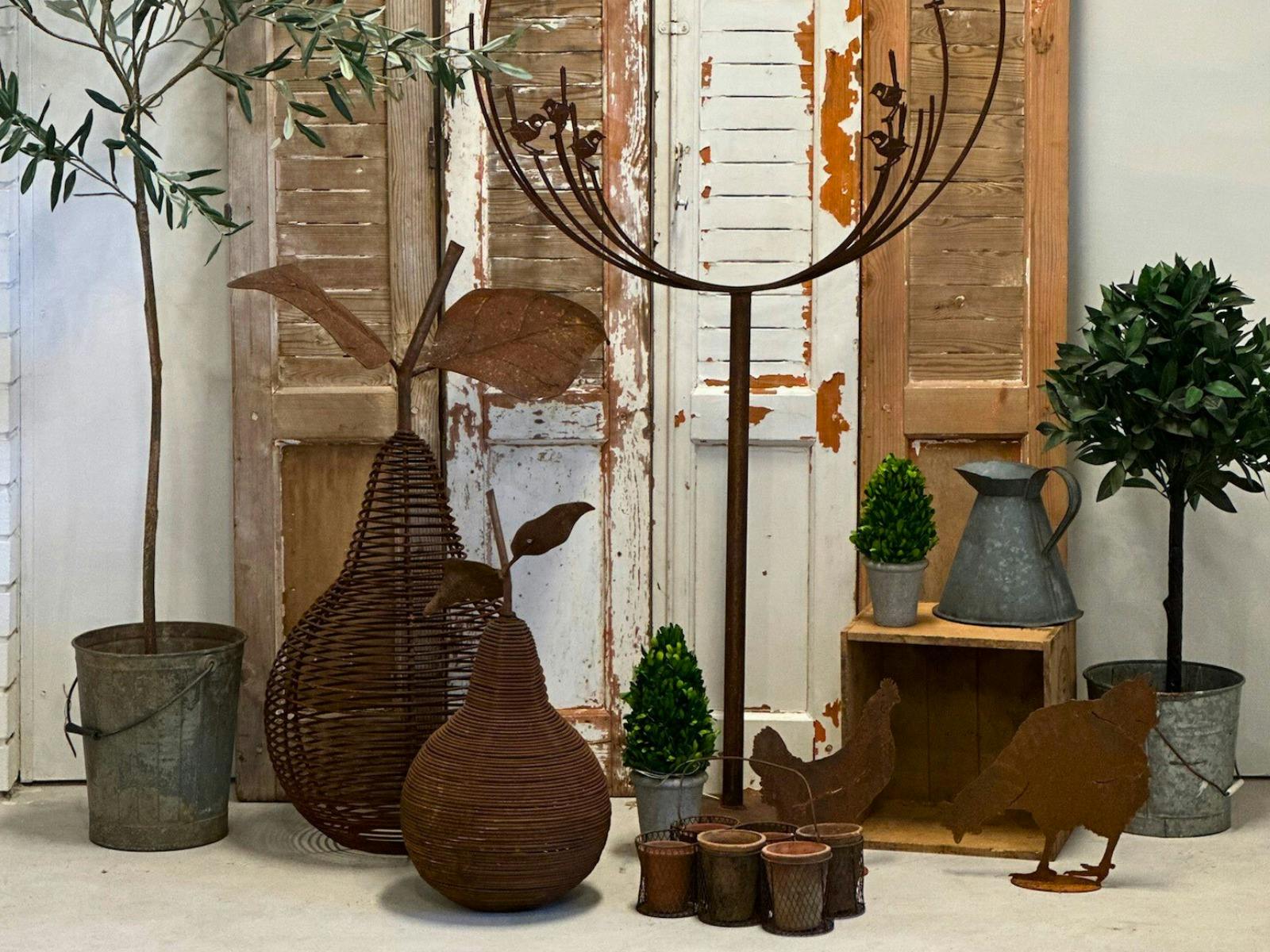 ヴィンテージのシャッターの前にある植物と大きな錆びた金属製の洋ナシの形、亜鉛メッキのバケツ