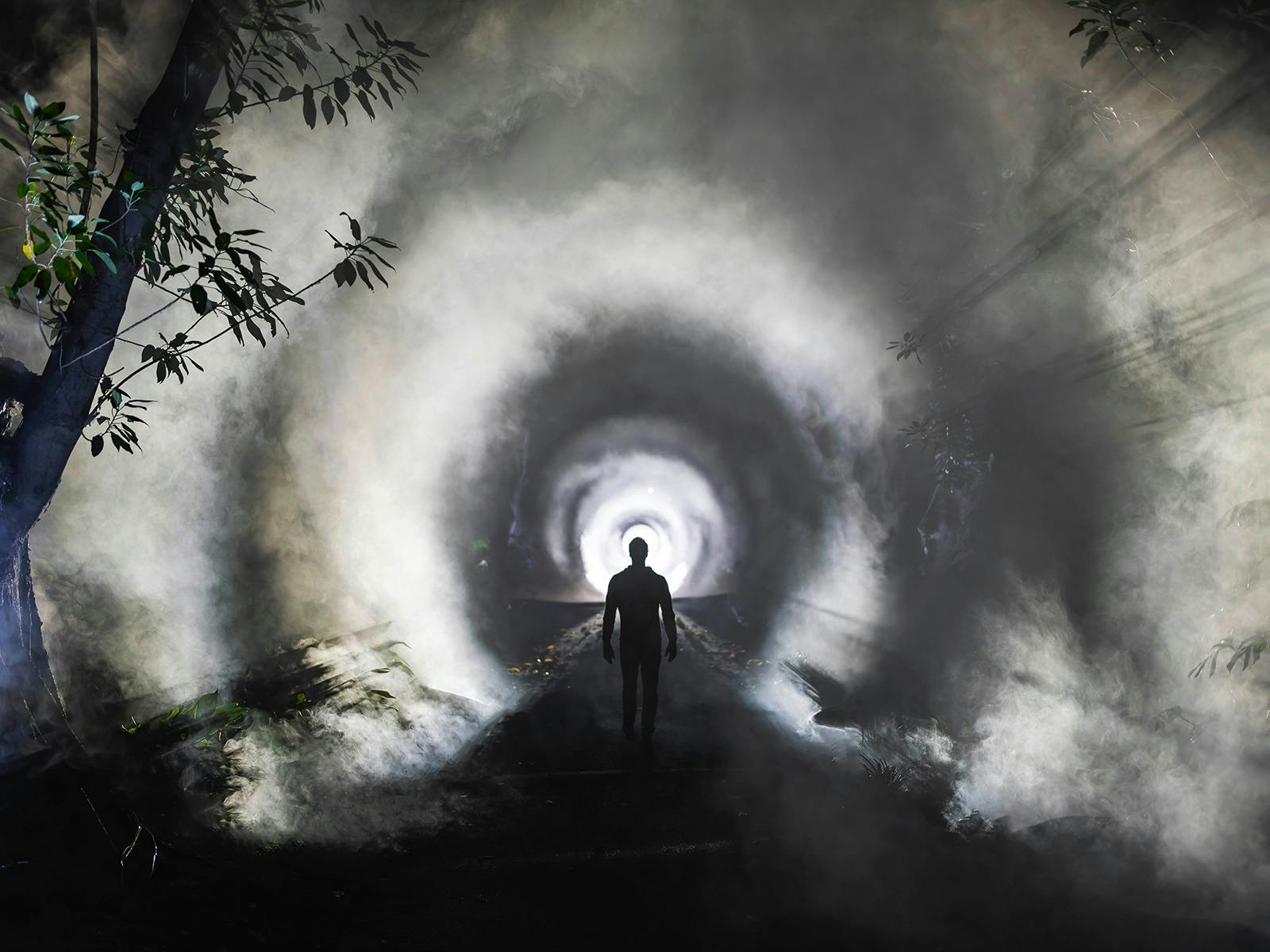 Human silouette walking down a path with haze and lights creating a tunnel visual.