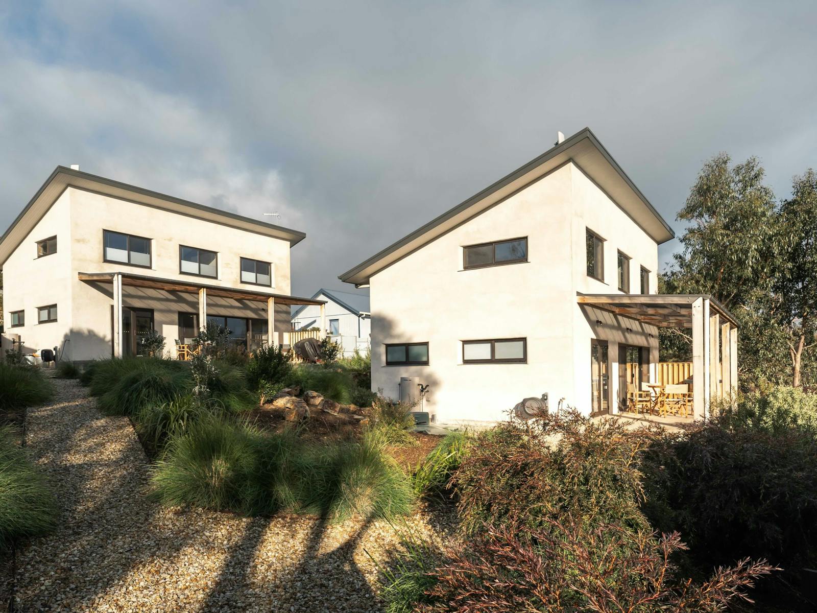 Two identical villas made from hempcrete surrounded by native gardens.