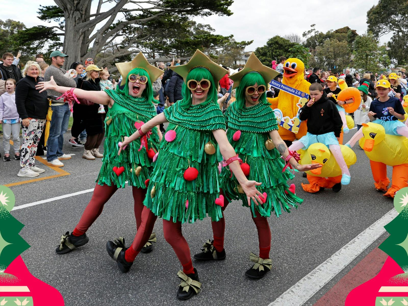Parade performers dressed as Christmas trees entertain crowds at a festive street parade.