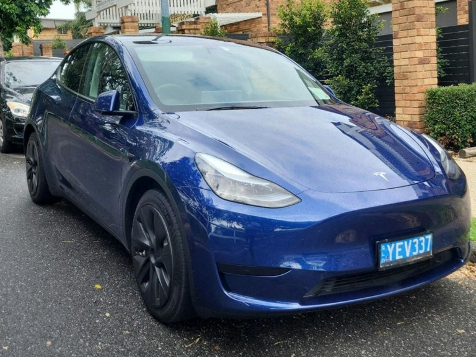 A Blue Model Y Tesla parked on a tarmac roadway
