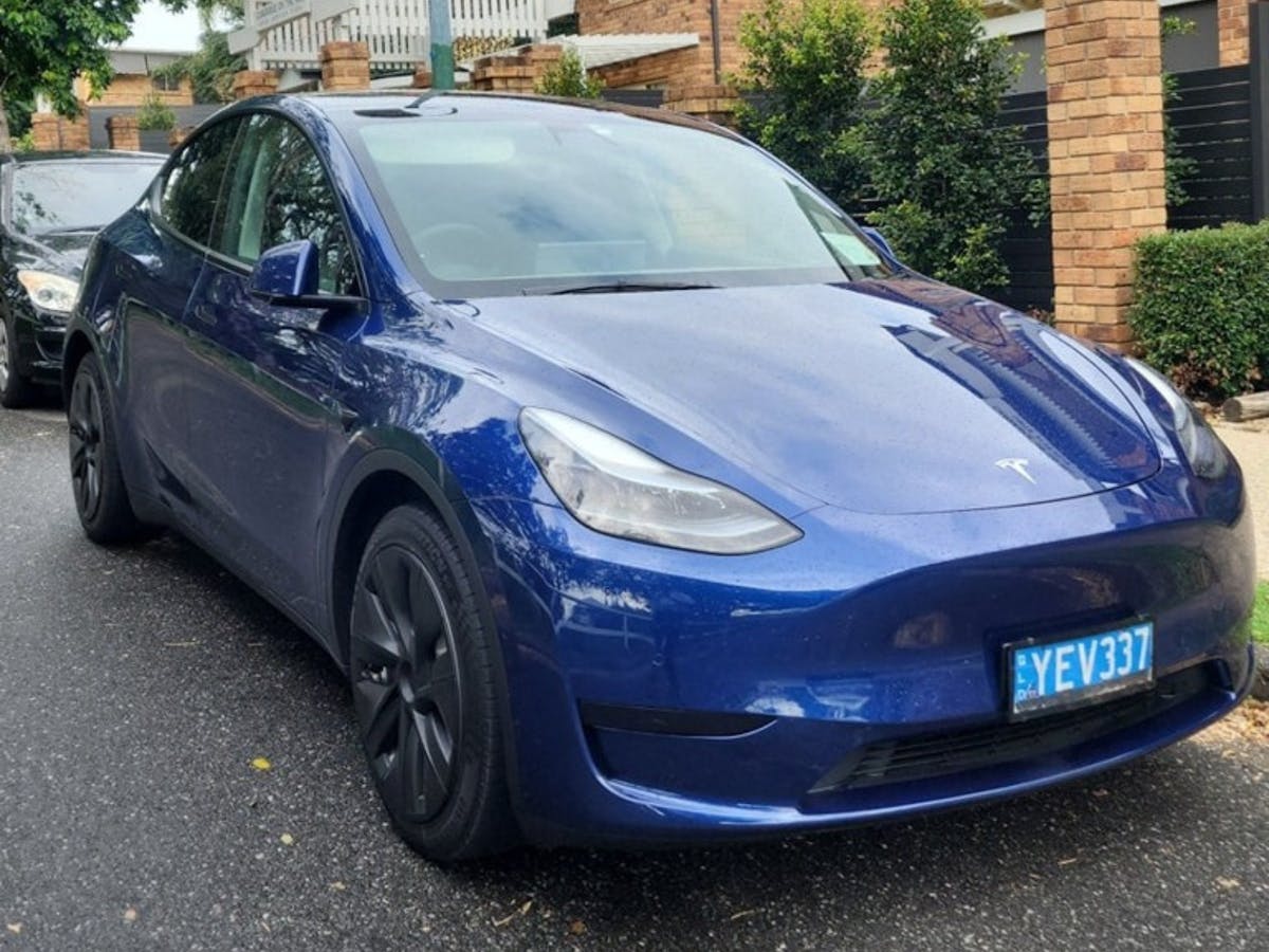 A Blue Model Y Tesla parked on a tarmac roadway