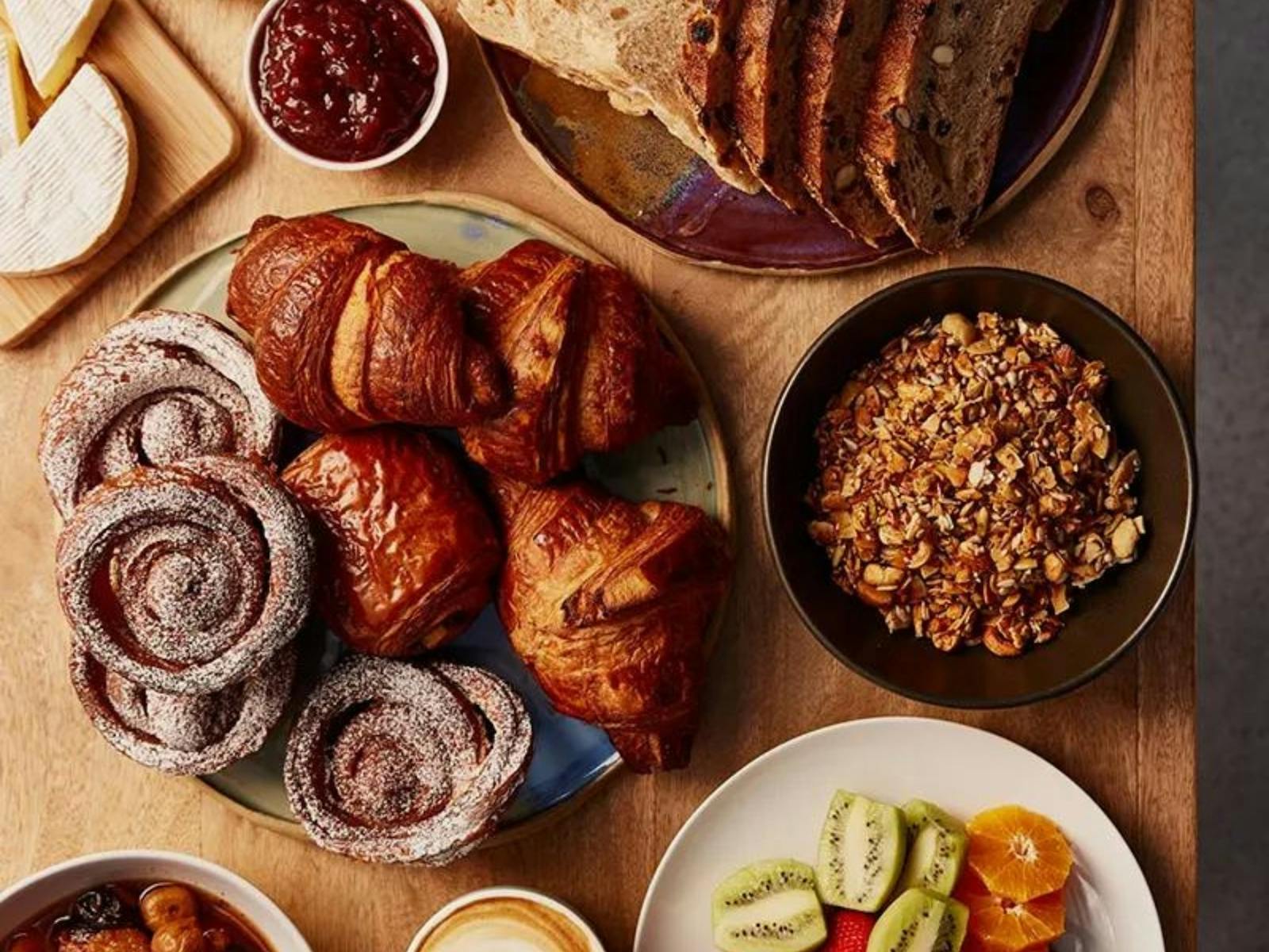 A table laden with pastries, granola, fruit, coffee, cheese, spreads and condiments.