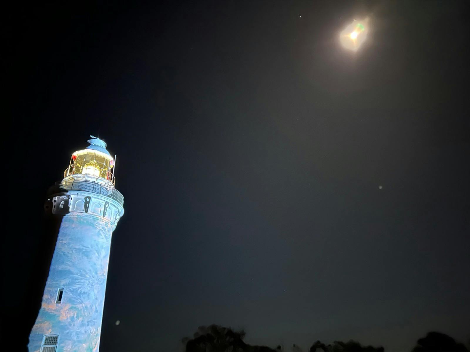 Image of lighthouse with projected image on it and the moonlight above.