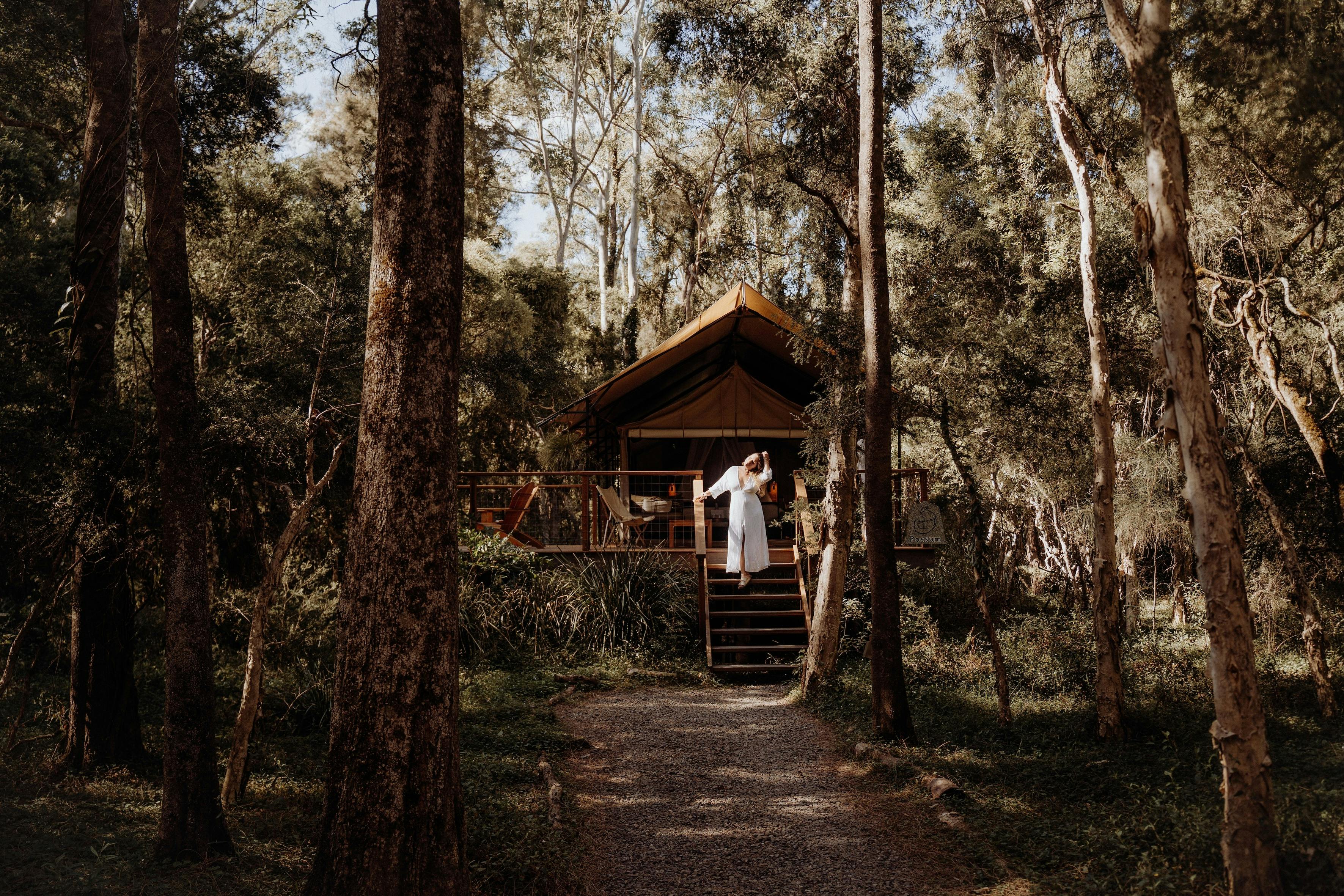 Safari tent and woman looking out to bush surrounds from verandah