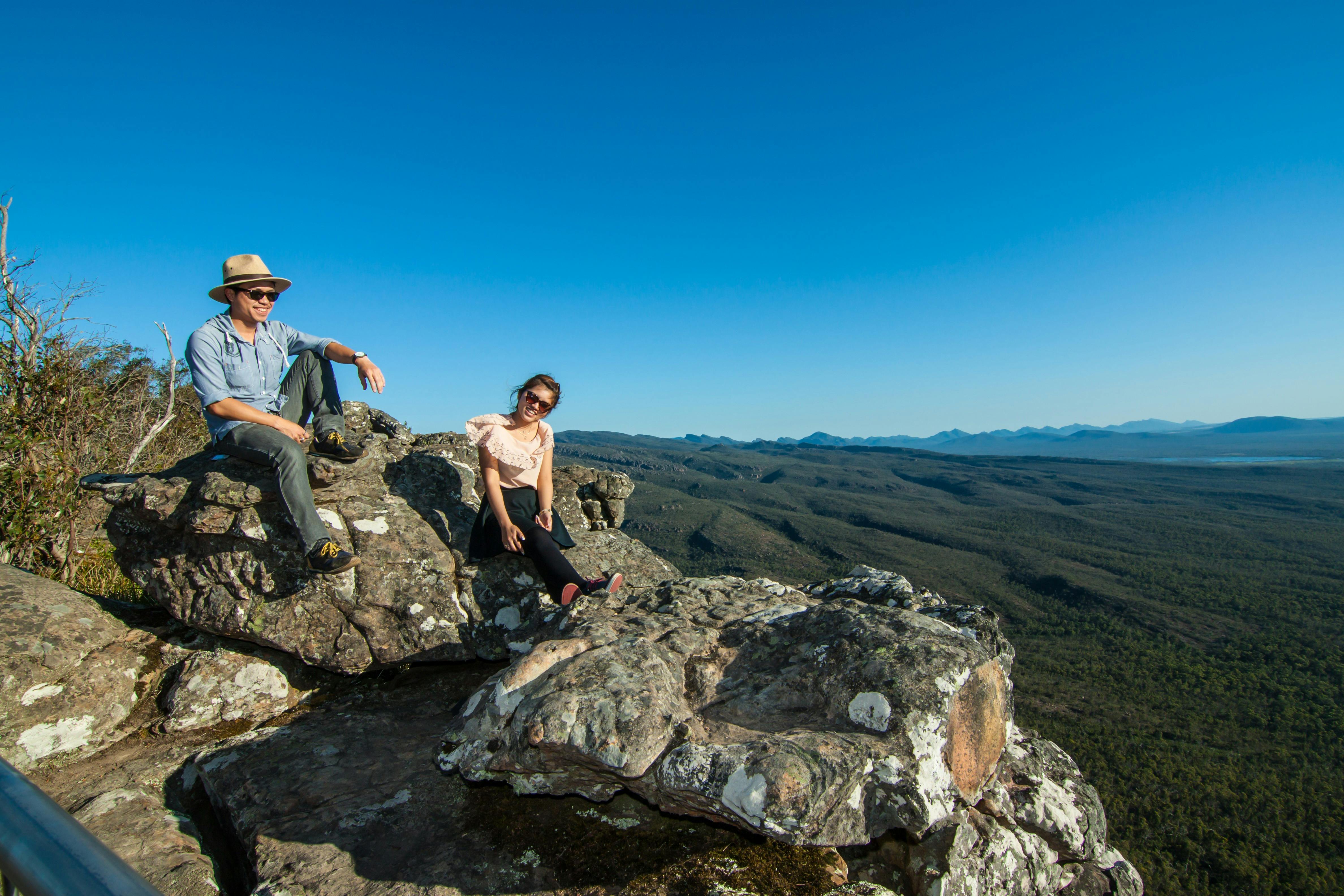 A couple sitting on a rock ledge at the Grampians, with a clear blue sky