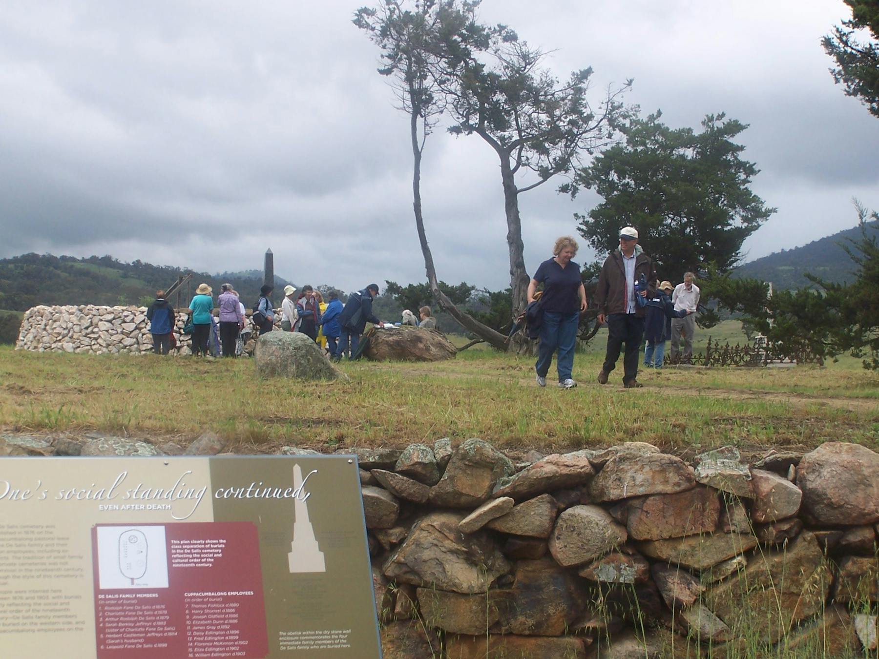 People walking on raised ground with stone wall and sign