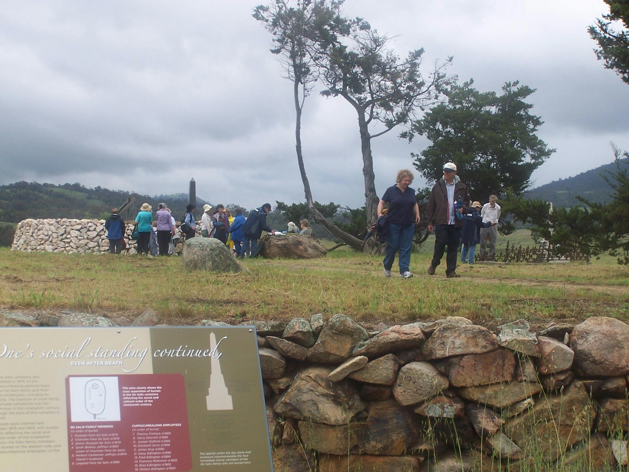 People walking on raised ground with stone wall and sign