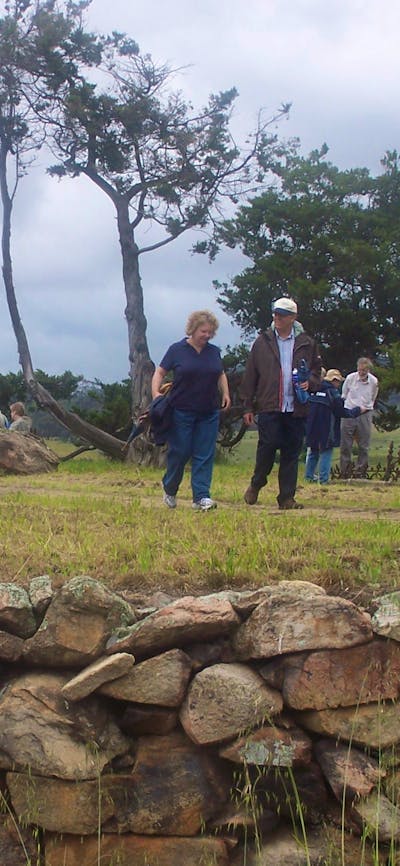 People walking on raised ground with stone wall and sign