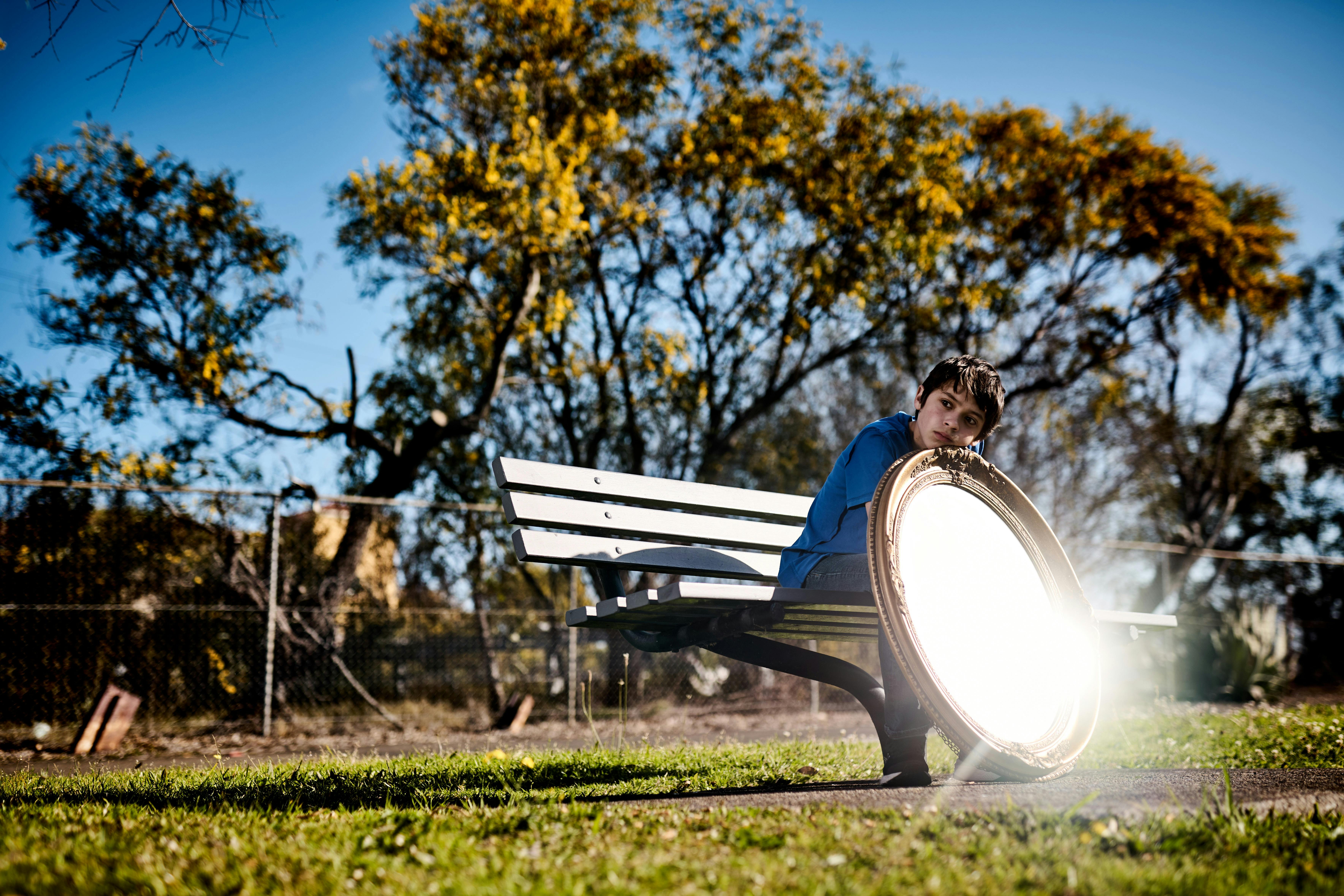 A Young Person sitting in a park with a mirror reflecting light