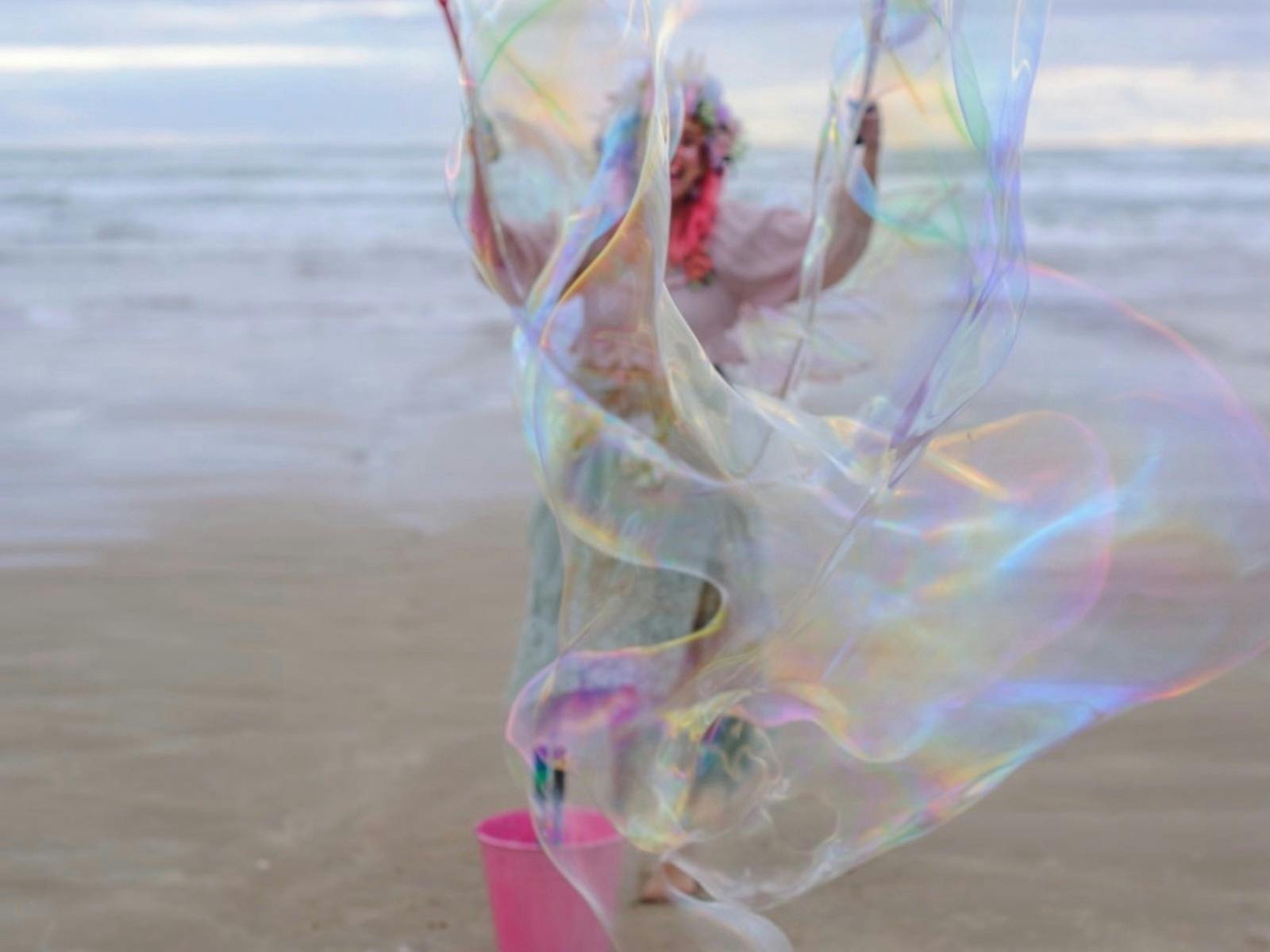 A giant translucent bubble obscuring the creator on a sandbeach