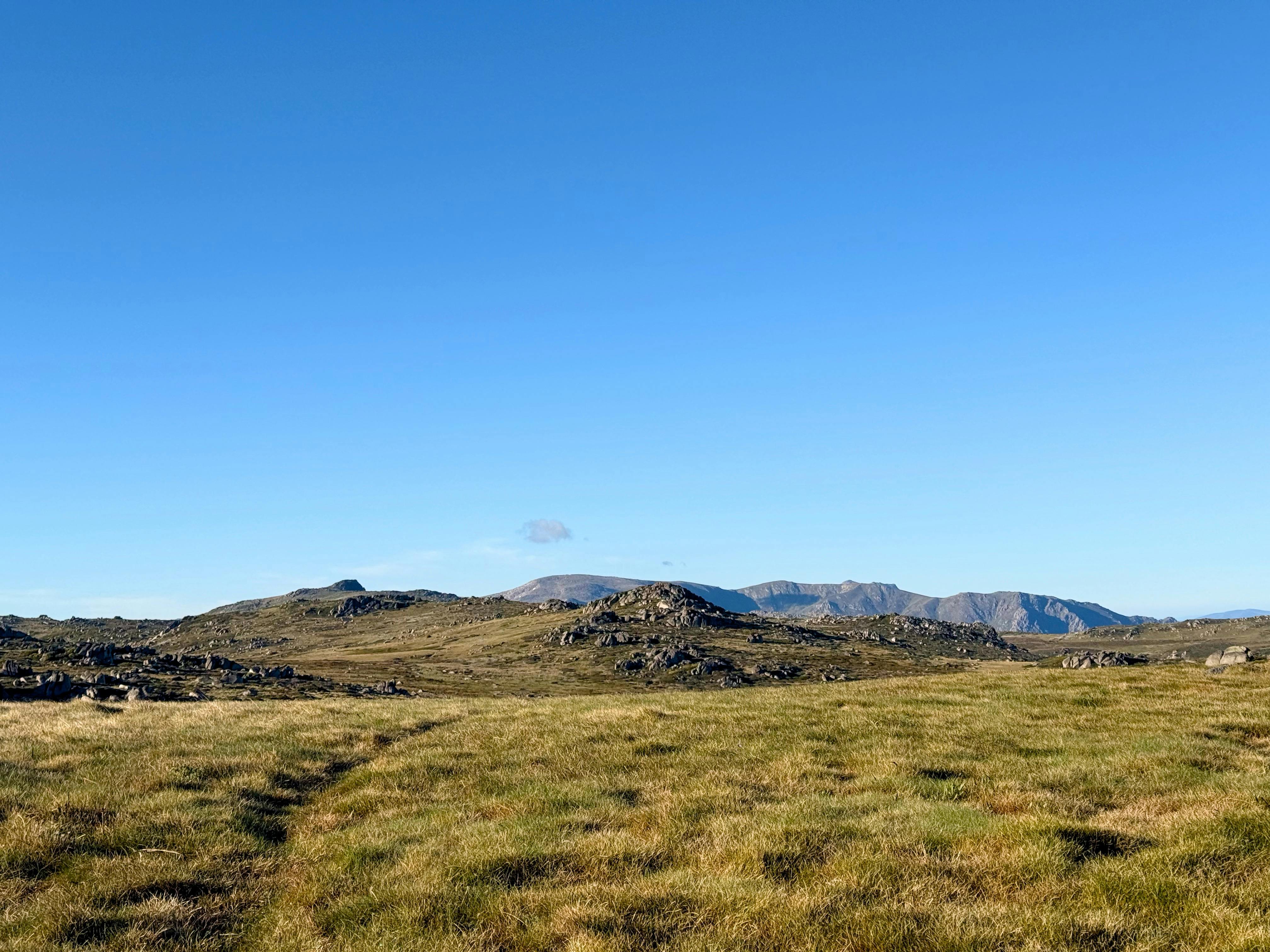 A wide open rolling mountain with bigger mountains in the distance.