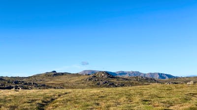 A wide open rolling mountain with bigger mountains in the distance.