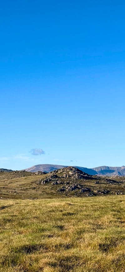 A wide open rolling mountain with bigger mountains in the distance.