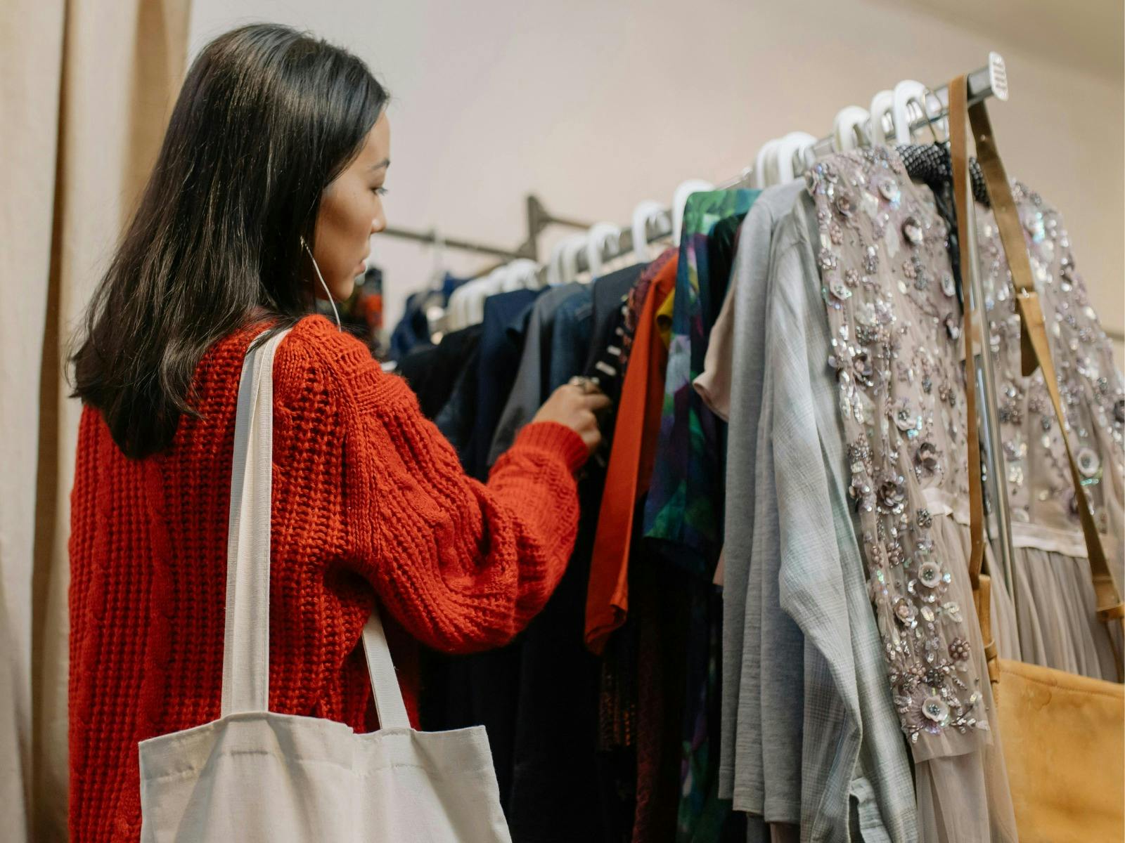 Young woman in red jumper sorts through vintage clothing rack