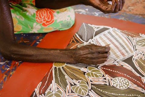 Aboriginal artist Joy Borruwa sitting on the floor painting