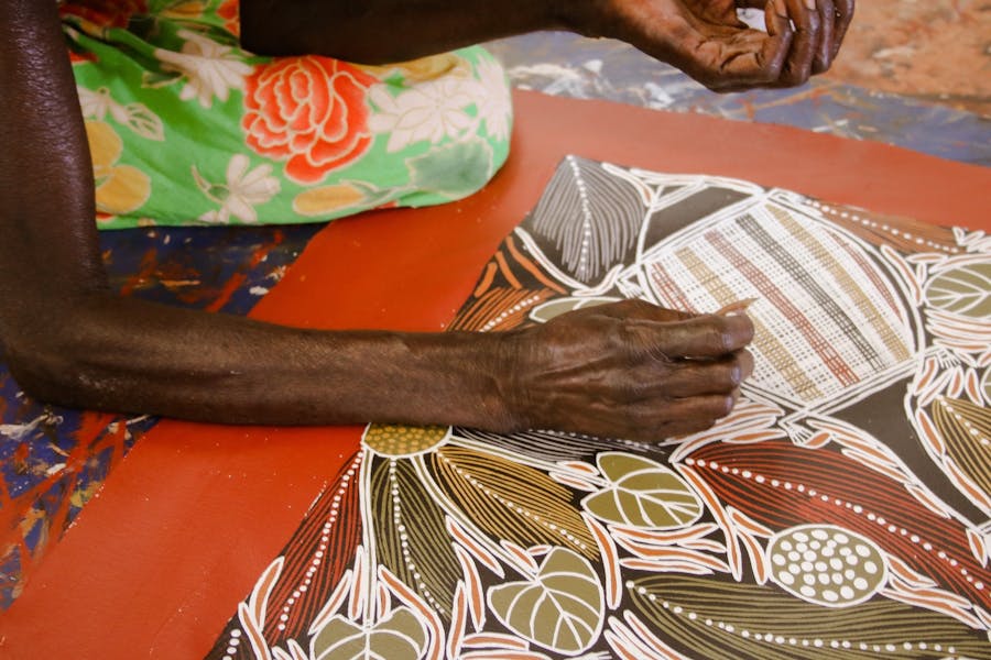 Aboriginal artist Joy Borruwa sitting on the floor painting