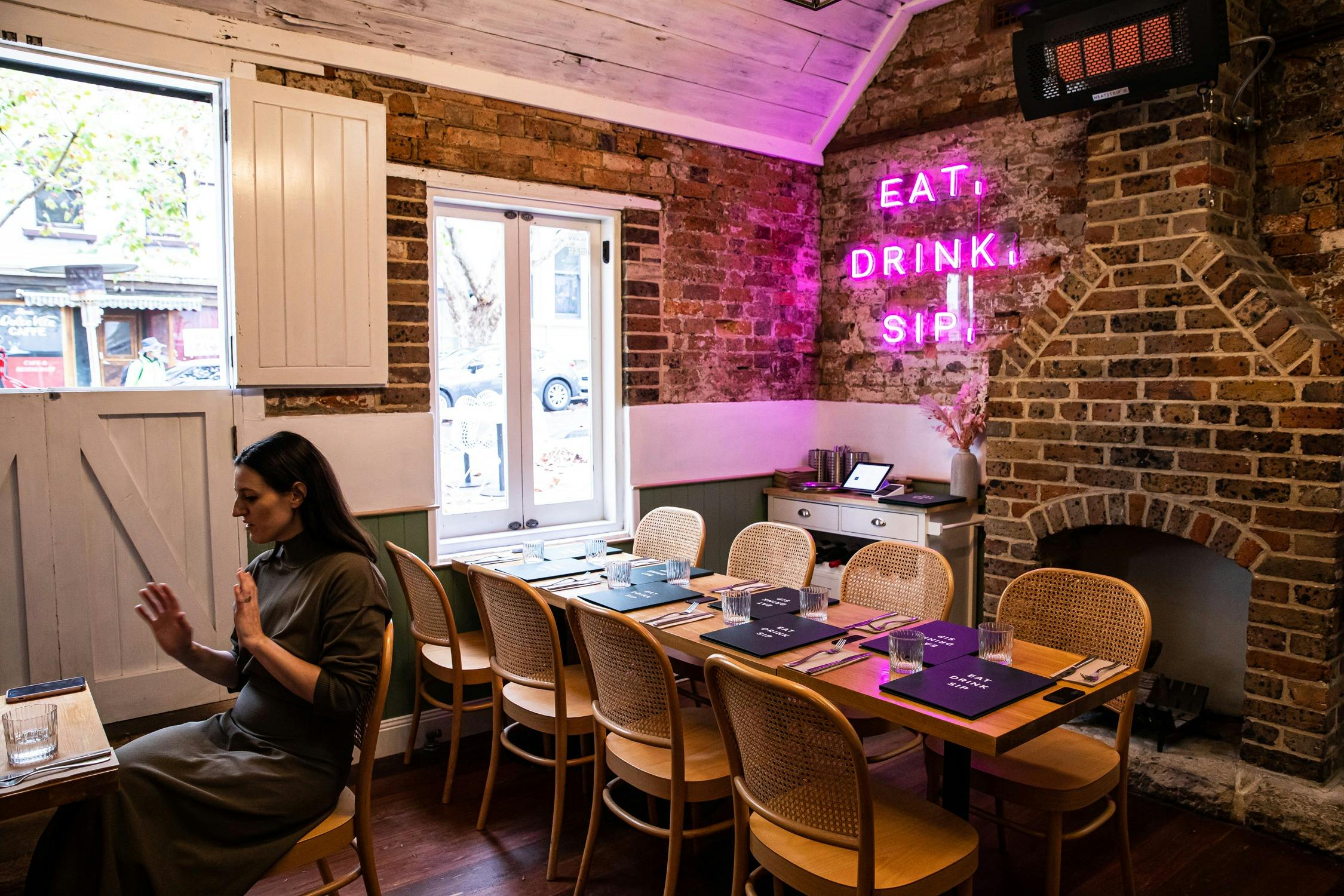 Cosy indoor dining area within sandstone cottage, with neon sign saying Eat Drink Play