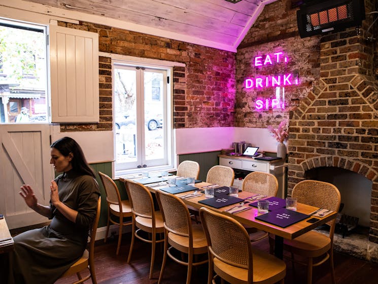 Cosy indoor dining area within sandstone cottage, with neon sign saying Eat Drink Play