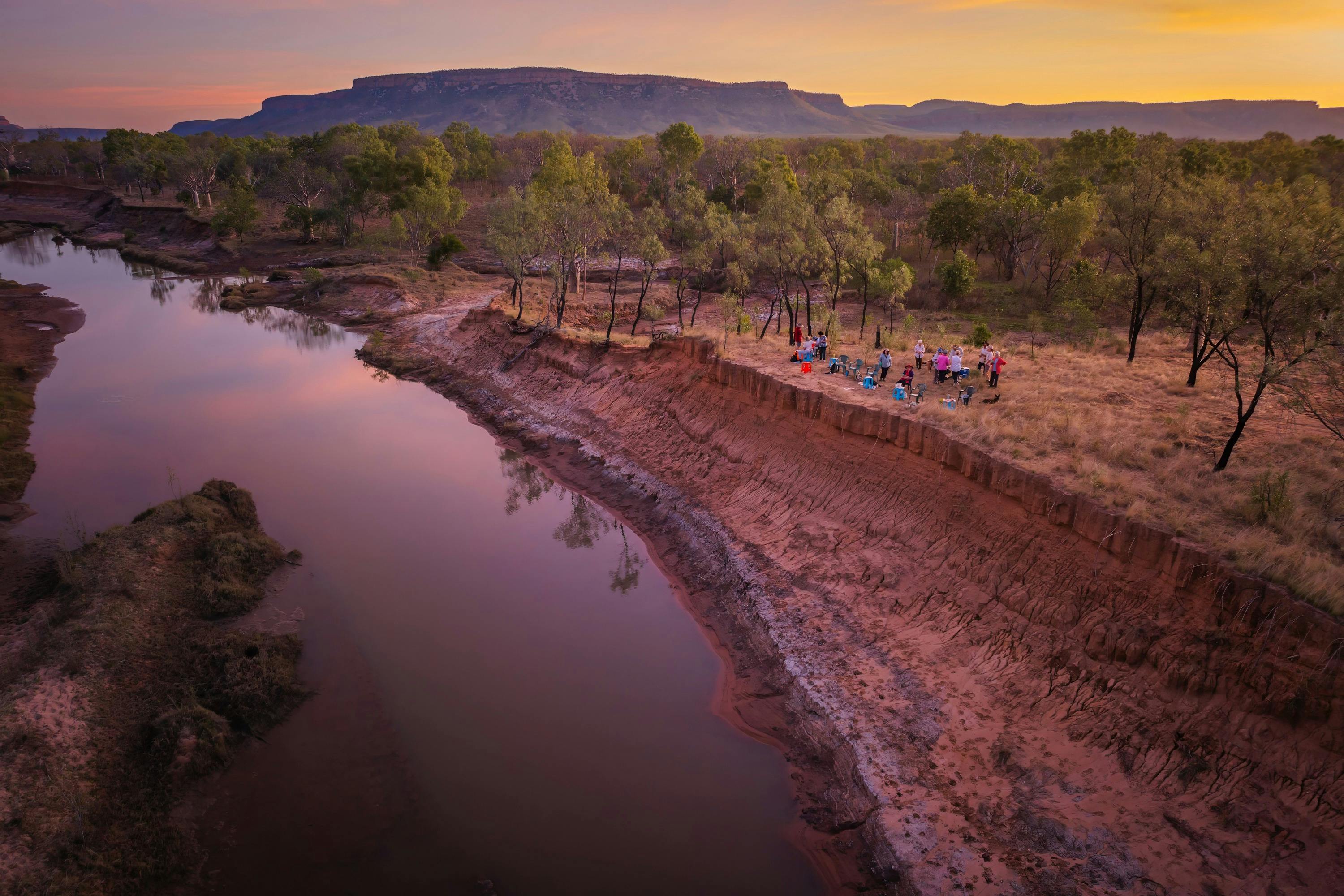Aerial view of a group of people on a bank beside a river at sunset